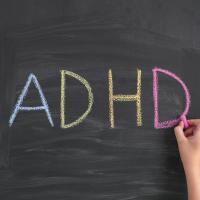 Child's hand writing ADHD on a chalkboard
