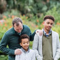 A man and his two sons. The older son looks unhappy.