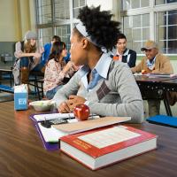 Teen sitting alone at a cafeteria table looking longingly at social group.