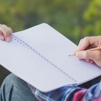 View of person's hands writing in notebook