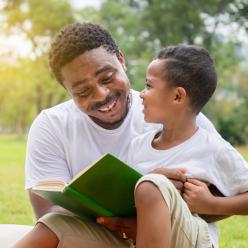A smiling father and son reading outside