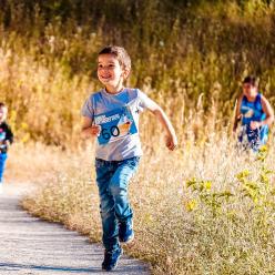 Young boys running down path through a field with racing numbers pinned to shirts