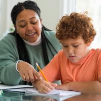 Tutor working with a young student at a table.
